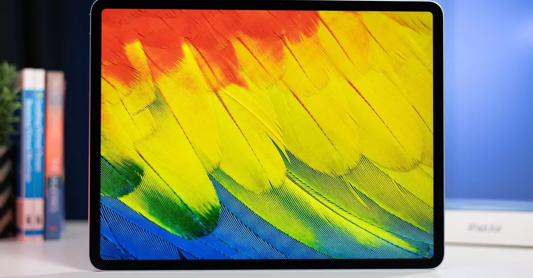 iPad Air M2 on a white table showcases an image of vibrant feathers on its display.