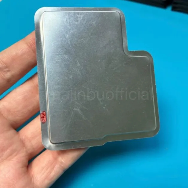 A person holding a metal heat sink or electronic component over a blue surface.