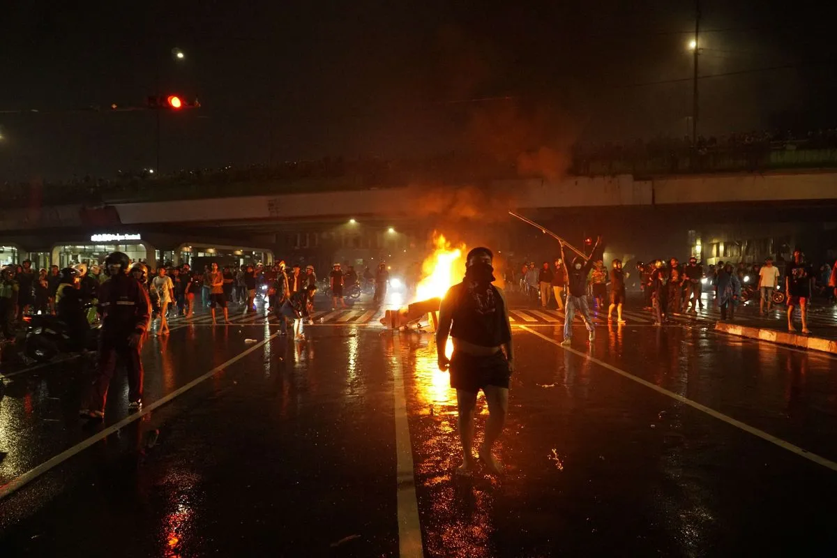 Pengunjuk rasa melintas di depan tumpukan barang yang terbakar saat aksi di depan Mako Brimob Kwitang, Jakarta, Jumat (29/8/2025). Massa menggeruduk Mako Brimob Kwitang menyusul peristiwa meninggalnya pengemudi ojek online (ojol) karena terlindas kendaraan taktis saat demonstrasi di depan DPR-RI pada Kamis, 28 Agustus.