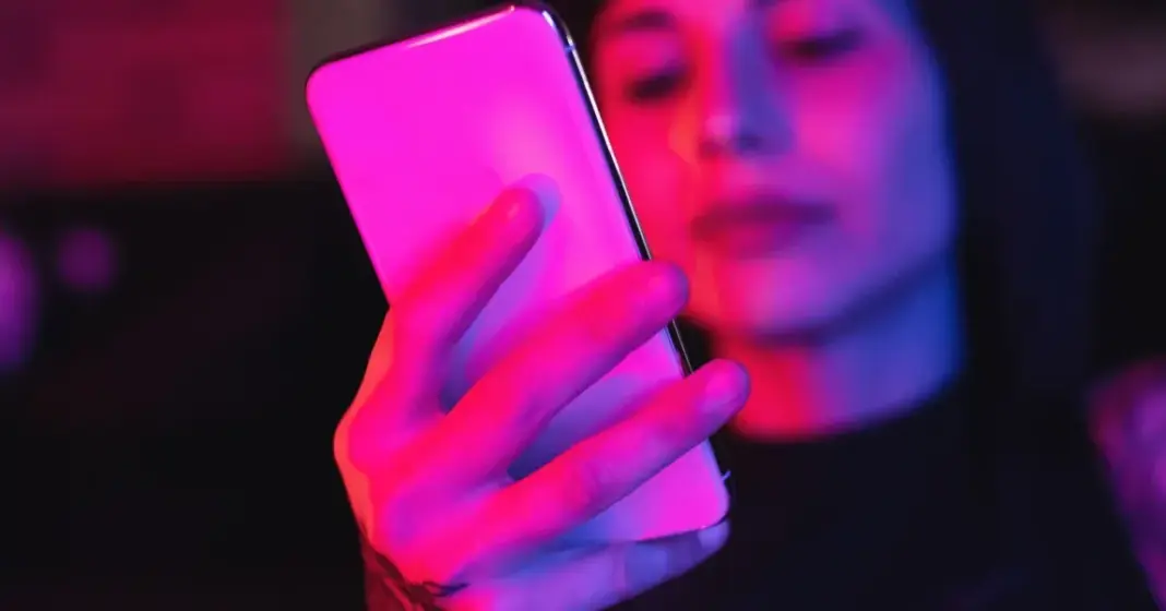 Wanita menggunakan ponsel dengan cahaya pink, simbol interaksi manusia dengan teknologi AI