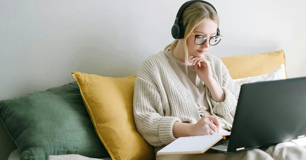 Wanita menggunakan laptop dengan headphone di latar belakang yang nyaman, representasi aktivitas kuliah
