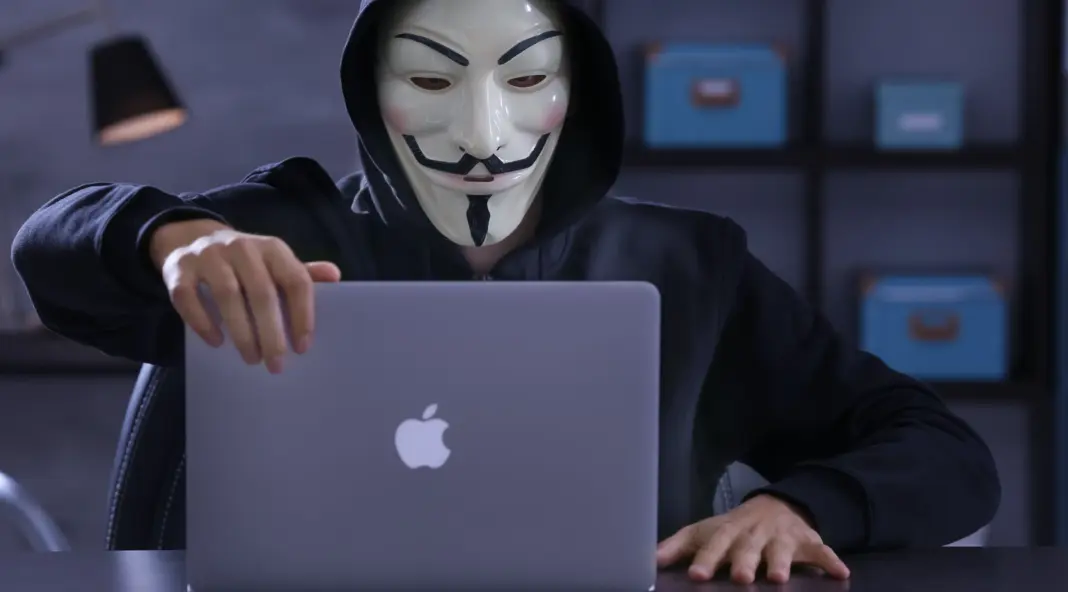 Peretas dengan topeng Guy Fawkes menggunakan Apple MacBook untuk kegiatan ilegal