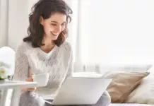 Happy woman sitting on a bed with a coffee and a laptop using Windows 11