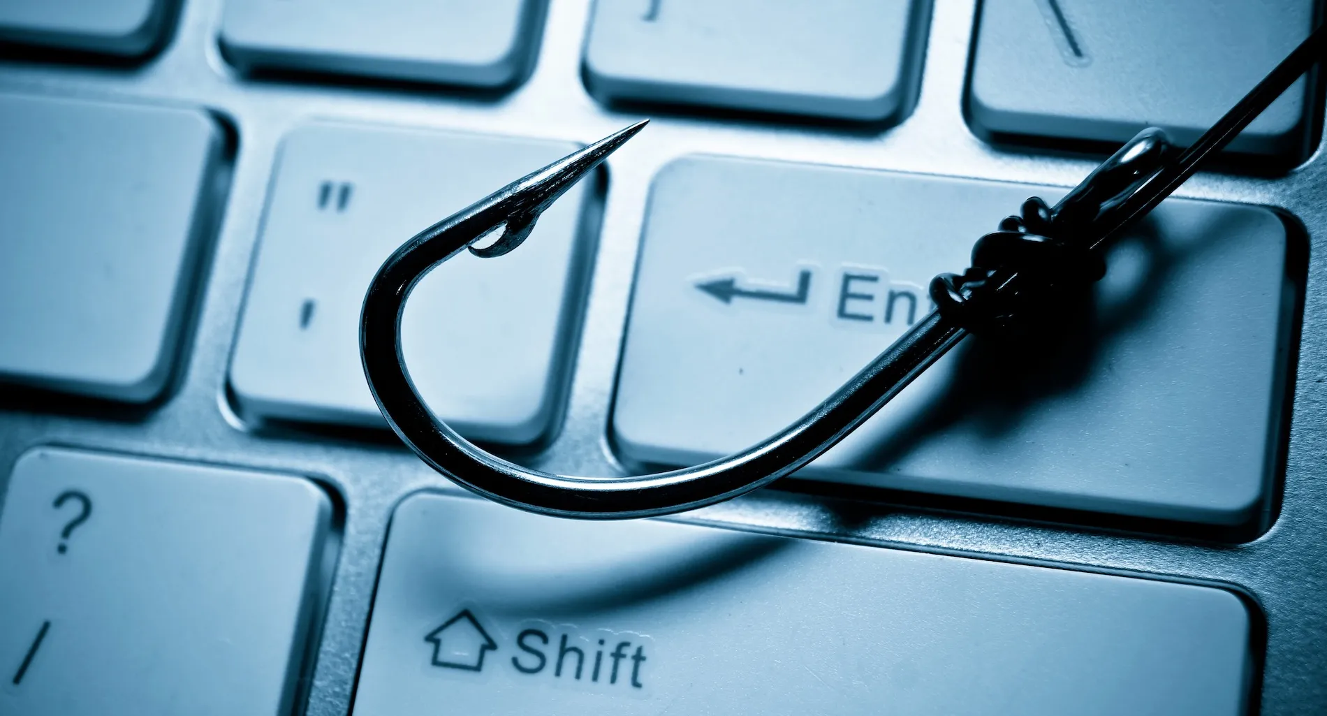 A fish hook is lying across a computer keyboard, representing a phishing attack on a computer system
