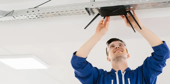 Man in blue jacket installing a router on ceiling
