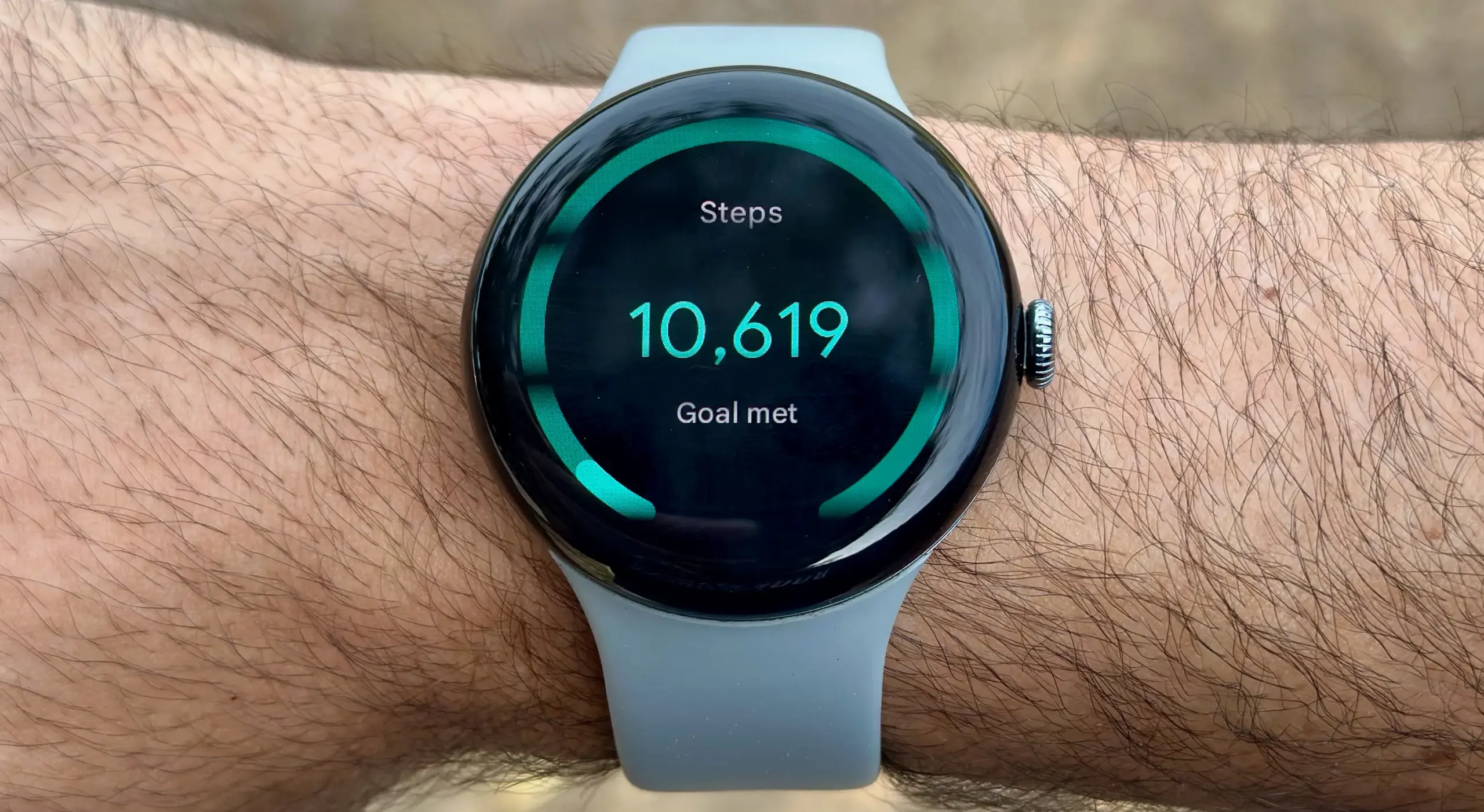 The Google Pixel Watch 3 on a wrist showing the Steps Tile, with 10,619 steps (Goal met)