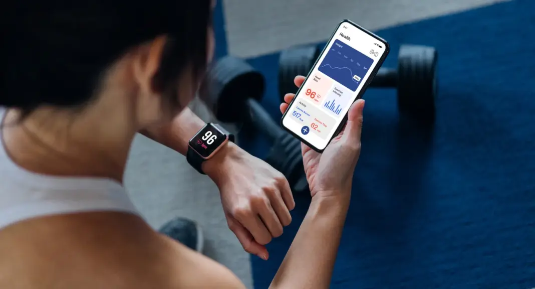Wanita menggunakan aplikasi workout di smartphone sambil menyinkronkan dengan smartwatch untuk memantau progres latihan