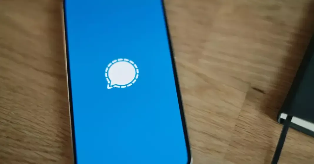 iPhone dengan layar loading aplikasi Signal yang menampilkan fitur cadangan cloud terbaru