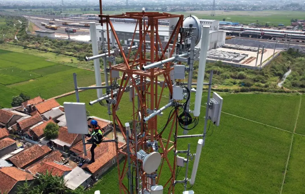 Menara pemancar sinyal internet berdiri tinggi di langit biru dengan awan putih, simbol infrastruktur telekomunikasi.