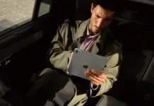 iPad Pro M5 dalam warna Space Black dengan layar OLED yang menampilkan wallpaper berwarna-warni, diletakkan di atas permukaan kayu.