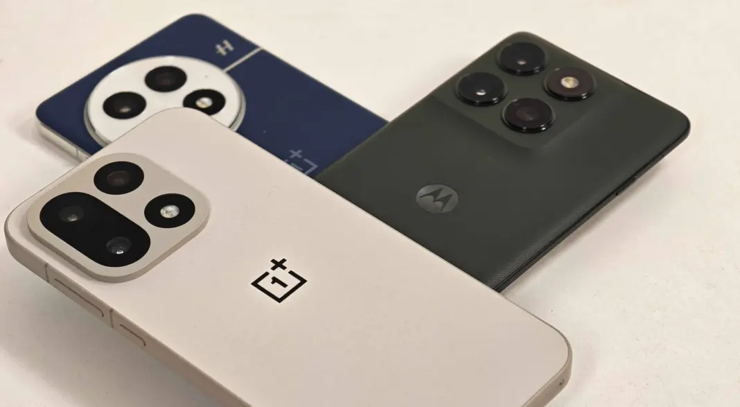Perbandingan visual smartphone OnePlus 13 dan OnePlus 15 dengan Motorola Edge 2025 di atas permukaan kayu.