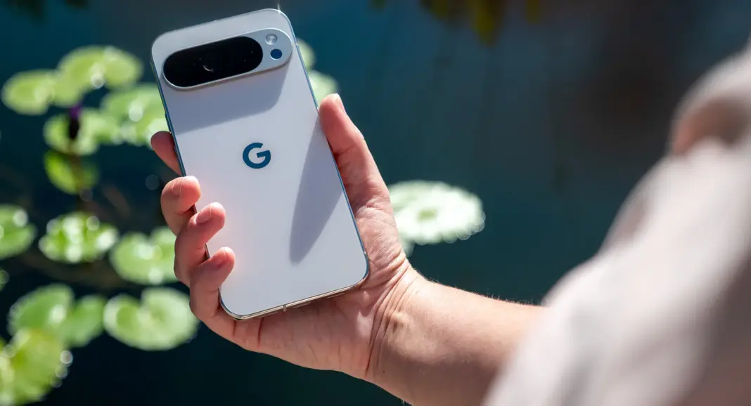 Google Pixel 10 Pro XL warna putih dipegang di depan kolam dengan daun teratai, menunjukkan desain premium perangkat.