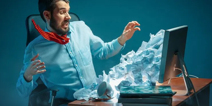 A man shocked by papers pouring out of his computer screen.