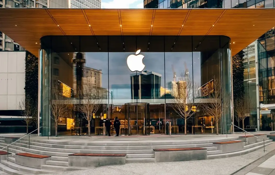 Ilustrasi logo Apple di tengah latar belakang sirkuit elektronik yang merepresentasikan dunia digital dan teknologi.