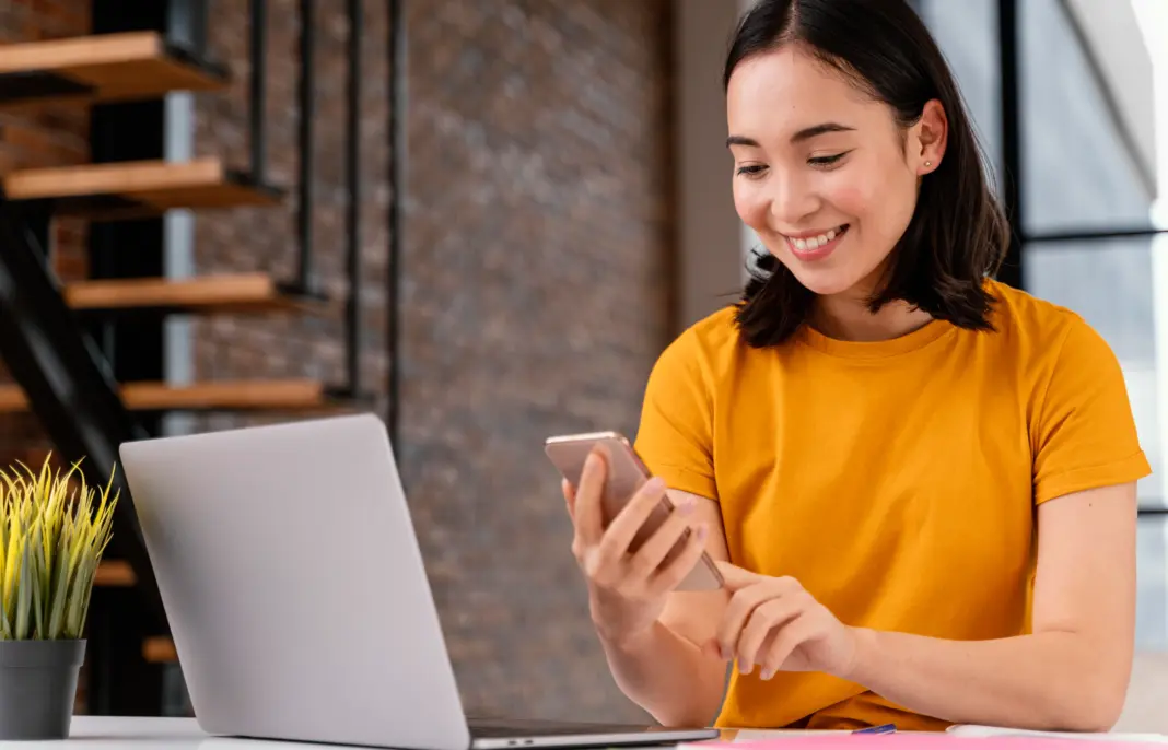 Wanita muda menggunakan ponsel dan laptop untuk mempersiapkan pembelian tiket konser online (cara war tiket konser) dengan serius.